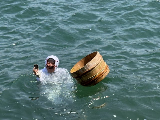 ミキモト真珠島の海女の実演で貝を手に海面へ浮かび上がる海女さん